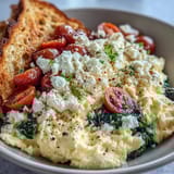 Warm scrambled eggs topped with sautéed spinach and crumbled feta in a breakfast bowl, served with whole grain toast.