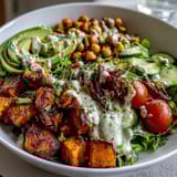Colorful Breakfast Buddha Bowl featuring roasted sweet potatoes, golden chickpeas, and fresh vegetables on greens with a drizzle of tahini dressing.
