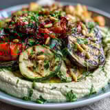 Vibrant Mediterranean veggie platter with smoky grilled vegetables and smooth hummus, garnished with parsley and pine nuts for a fresh, satisfying appetizer.  