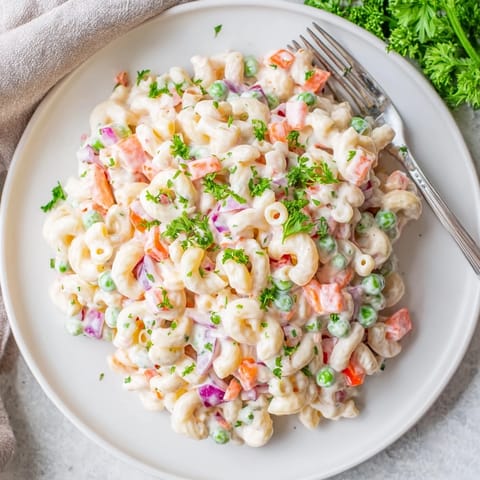 Chilled Macaroni Salad tossed with red peppers, peas, and fresh herbs, served on a picnic table.
