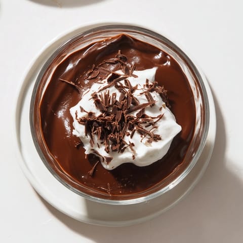 Creamy chocolate pudding in a glass, topped with a dollop of whipped cream and chocolate shavings.