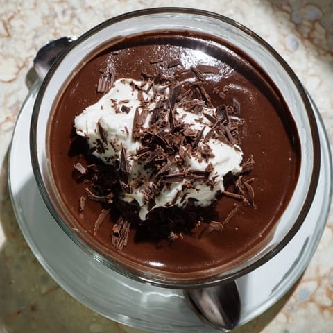 Rich chocolate pudding served chilled in a glass, garnished with fresh raspberries for a pop of color.