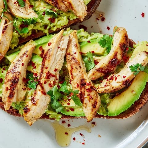 Slices of grilled chicken rest on golden sourdough toast spread with creamy smashed avocado, finished with a honey drizzle and chili flakes for a sweet-spicy finish.