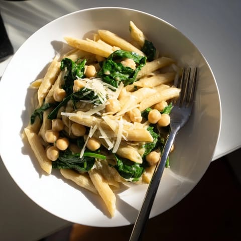 A hearty serving of Creamy Tuscan Chickpea Pasta garnished with fresh basil and grated Parmesan, perfect for a vegetarian family dinner.