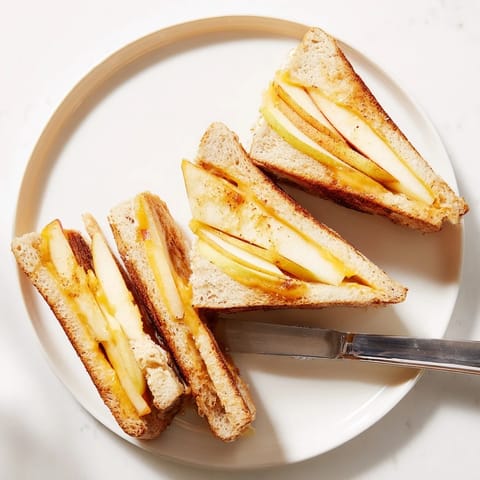 A close-up of Smoked Gouda & Apple Grilled Cheese showing thin apple slices, with a bowl of creamy tomato soup nearby.
