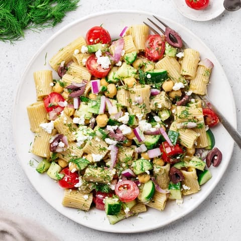 Zesty Mediterranean-inspired lemon herb chickpea pasta salad topped with crumbled feta and kalamata olives, perfect for a light, refreshing summer meal.