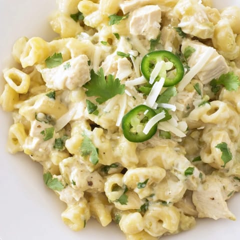 A close-up of Green Chili Chicken Mac in a cast-iron skillet highlights melted Monterey Jack and sharp cheddar cheese.  