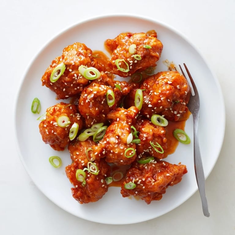 A close-up of golden-fried Orange Chicken pieces tossed in glossy citrus glaze, garnished with green onions and toasted sesame.