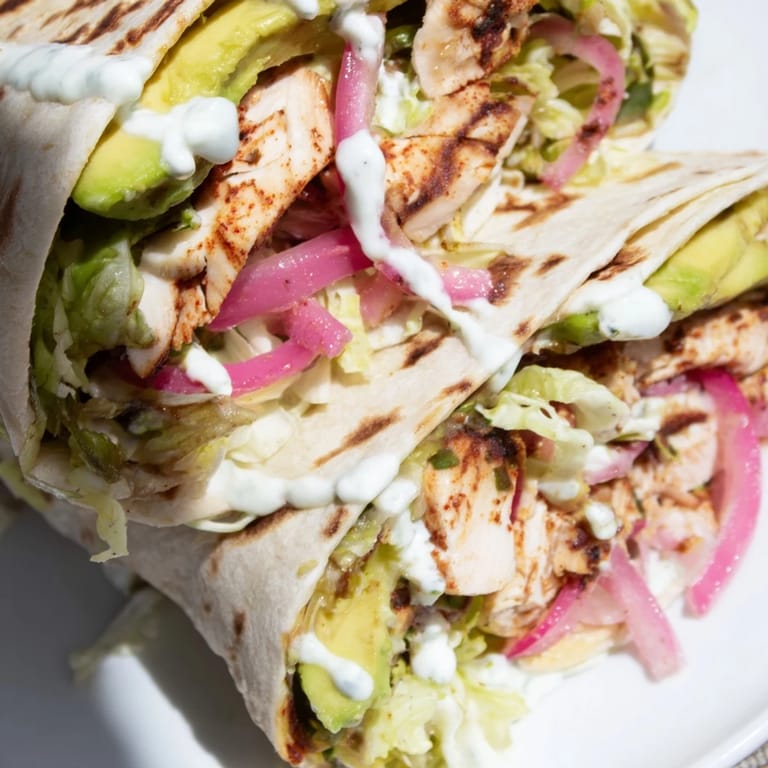 A close-up of the Smoky Chipotle Chicken Wrap cut in half, revealing juicy chicken and fresh vegetables inside the soft tortilla.