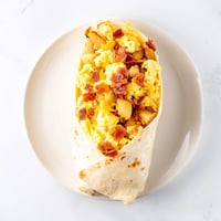 Golden-brown flour tortilla filled with fluffy scrambled eggs, crispy potatoes, melted cheddar, and savory bacon for a hearty Breakfast Burrito.