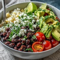 A bright overhead shot of a Black Bean and Veggie Bowl loaded with black beans, sweet corn, diced tomatoes, and creamy avocado.