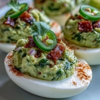 Creamy guacamole stuffed into classic deviled eggs, garnished with smoked paprika and fresh cilantro for a vibrant appetizer.